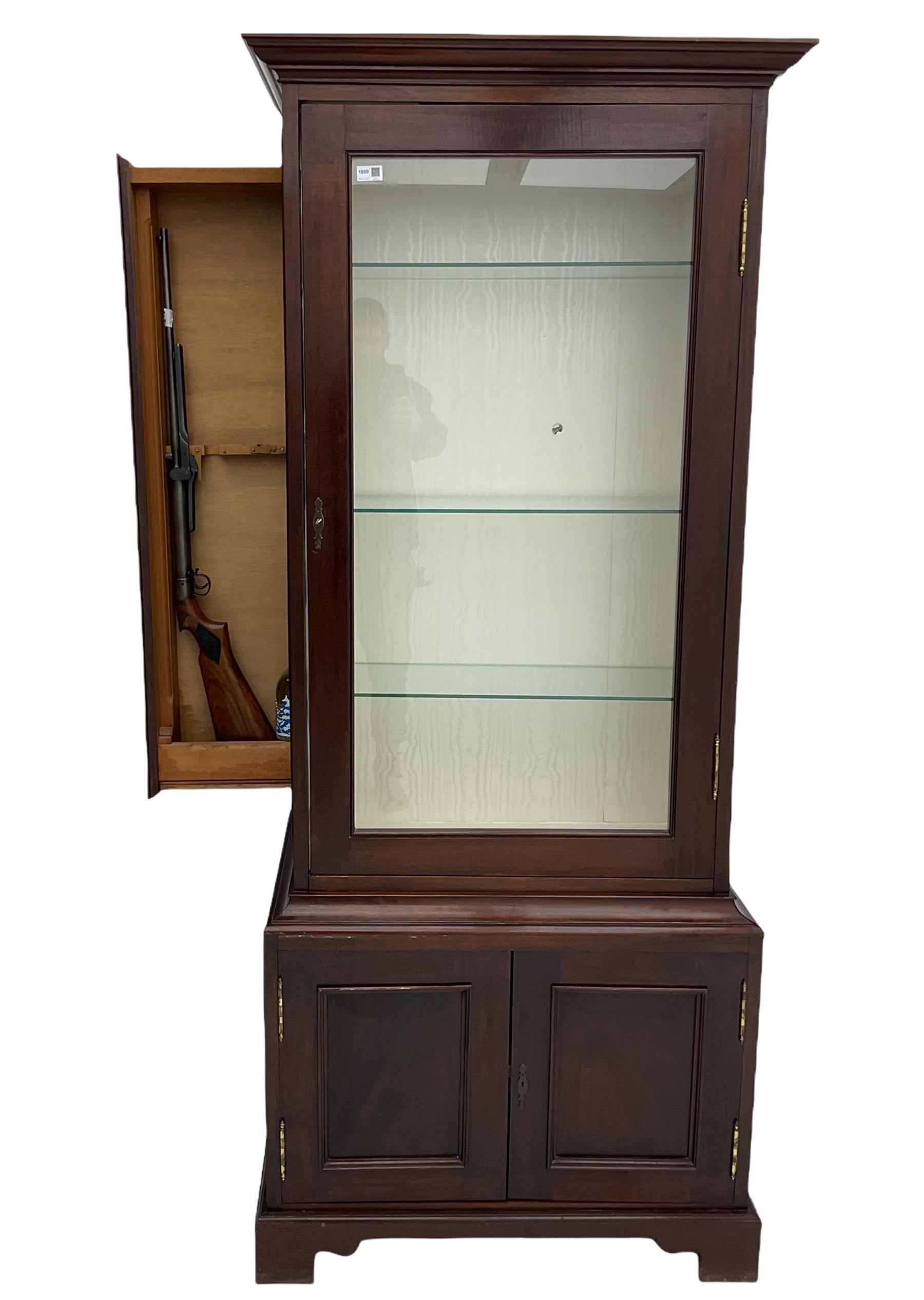 Mahogany display cabinet with hidden compartment, projecting cornice over single glazed door enclosing glass shelves, double panelled cupboard below, the interior with button releasing sliding back compartment, on bracket feet