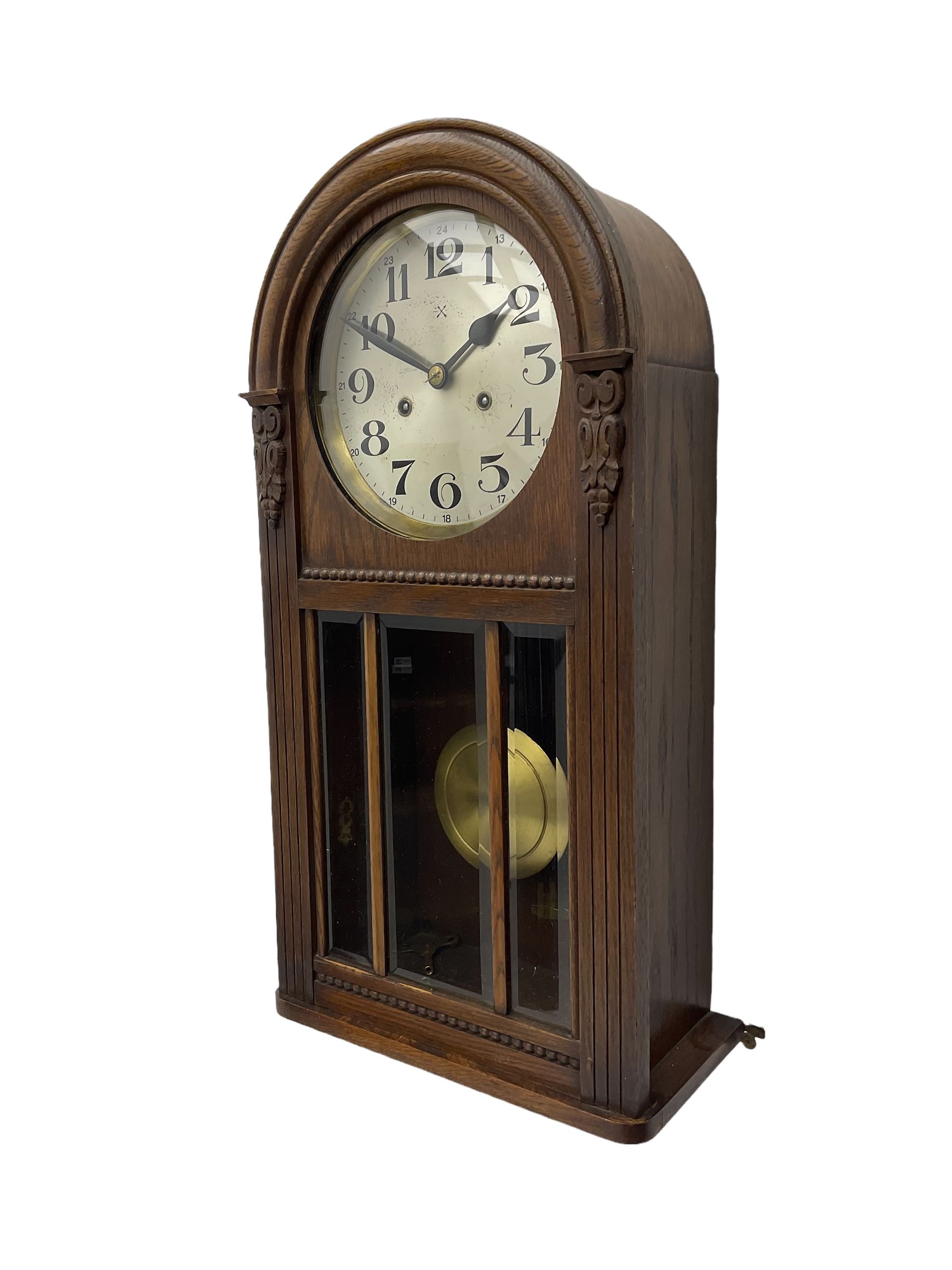 German HAC “ting tang” quarter striking wall clock in a round arched oak case with applied carving and beadwork, glazed door with a visible pendulum and silvered 24-hour dial with Arabic numerals and steel spade hands,  8-day spring driven movement striking on gong rods.

