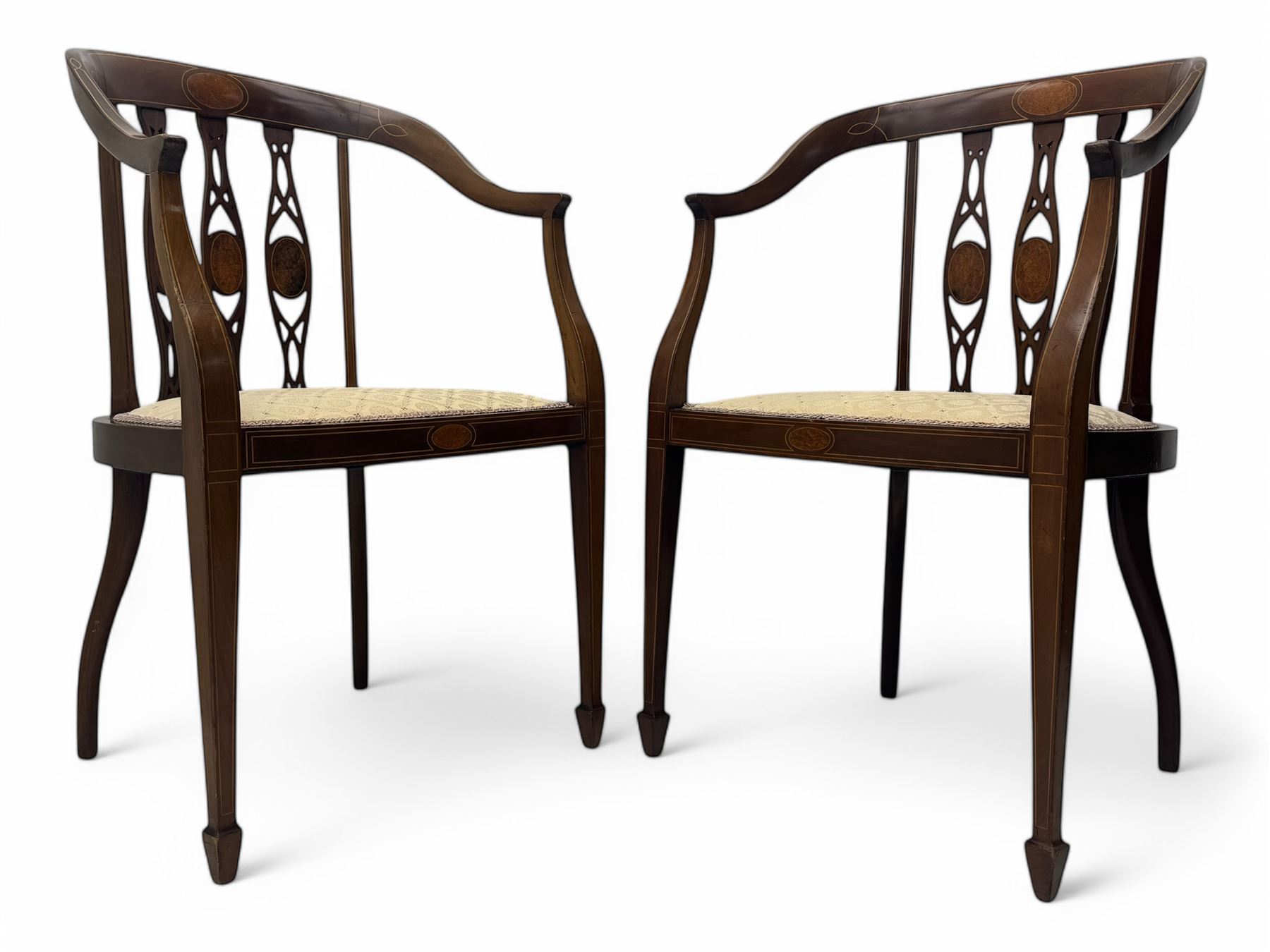 Pair of Edwardian mahogany tub chairs, curved top rail inlaid with oval marquetry panels, the backs with a pierced, elongated splat design featuring a central oval motif, the seats upholstered in cream fabric, on square tapering supports with spade feet