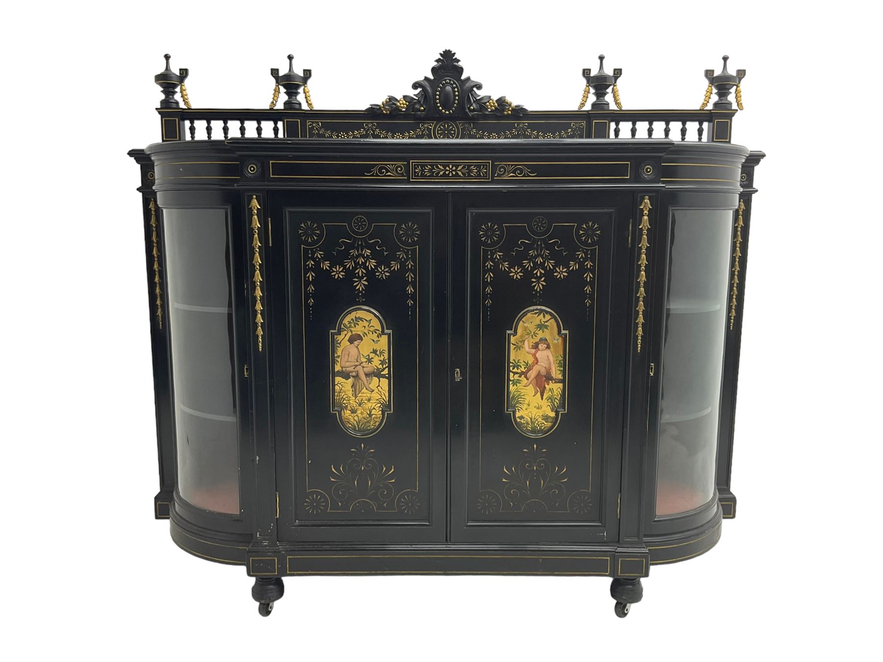 Victorian ebonised credenza side cabinet, raised balustrade back with urn finials and a central carved cartouche, carved and gilded with floral garland decoration, central doors with gilt panels painted with figures sitting over a lake enclosing two shelves, flanked by applied bellflower detail and glazed bow-front side doors, raised on ring turned feet with castors