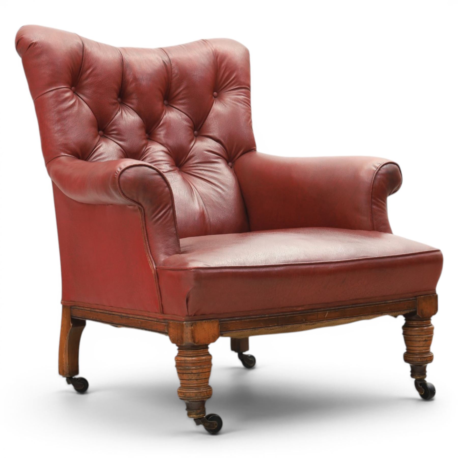 Early 20th century style oxblood red leather Chesterfield armchair, deep buttoned shaped back over padded scroll arms and loose seat cushion, raised on turned mahogany front supports with brass caps and castors