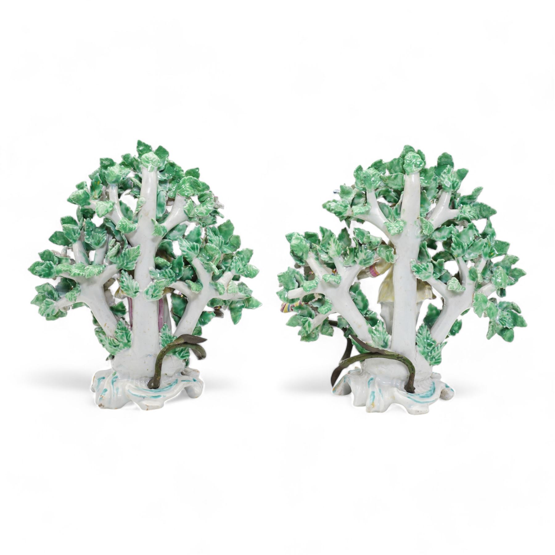 Pair of Bow porcelain 'New Dancers' candlesticks, standing before flowering bocages, and wearing brightly coloured flowered clothes, each supporting to left and right a tôle peinte branch terminating in a leaf moulded nozzle, on scrolling footed bases, red anchor and blue/red dagger marks beneath, H19cm x W18cm (2)