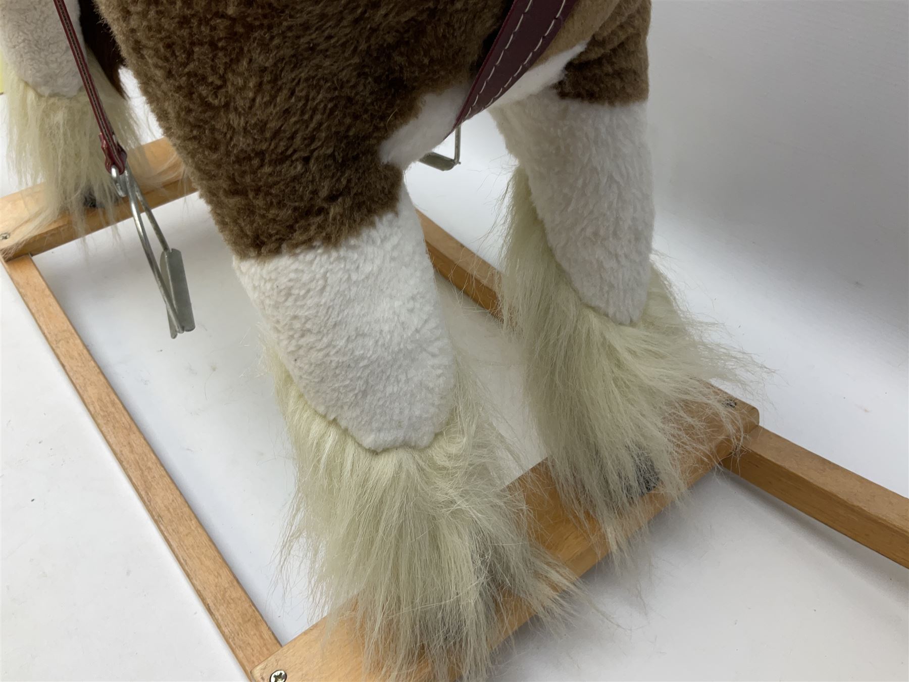 Modern plush covered rocking horse with inset eyes, simulated leather bridle and saddle with metal stirrups, on curving wooden rockers L94cm H64cm