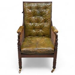 George IV mahogany framed library reading chair, reed moulded frame with cane work seat, back and sides, with loose cushions upholstered in green buttoned leather, upholstered arm rests, turned arm supports terminating to turned and reed carved feet, on castors 