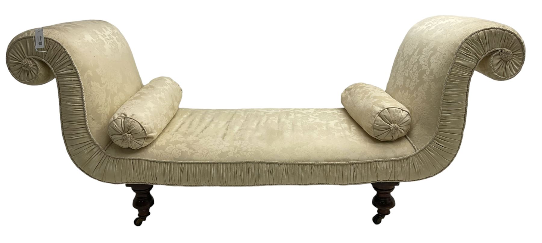 Victorian mahogany framed window seat day bed, the scrolled arms and seat upholstered in ivory foliate patterned damask fabric with matching ropetwist piping, raised on turned supports with castors