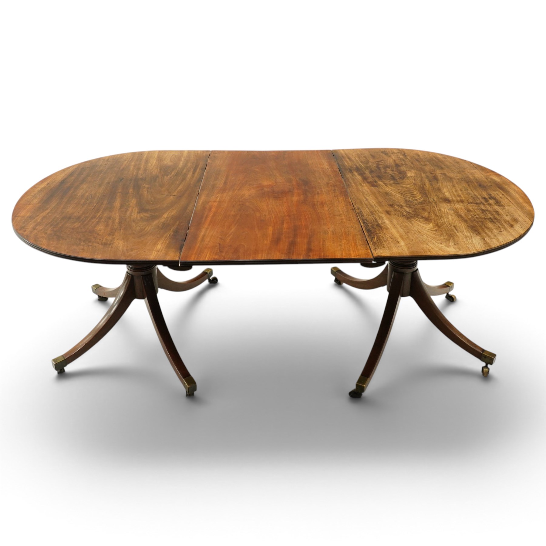 George III mahogany twin pedestal extending dining table, the twin D-ends with additional leaf, raised on twin turned pedestals terminating to four splayed supports with brass cups and castors