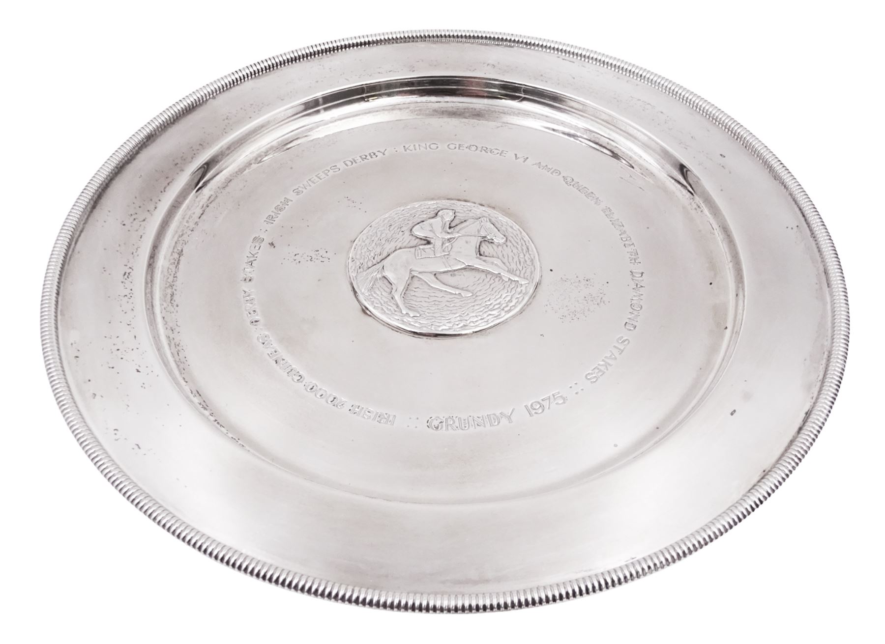 Modern limited edition silver salver, celebrating the achievements of Grundy, champion racehorse of 1975, each of circular form with gadrooned rim and plaque to centre depicting jockey mounted upon Grundy, designed by Stuart Devlin, limited edition no. 15/500, hallmarked London 1976, makers mark LH, D23cm, within silver lined fitted box and limited edition certificate 