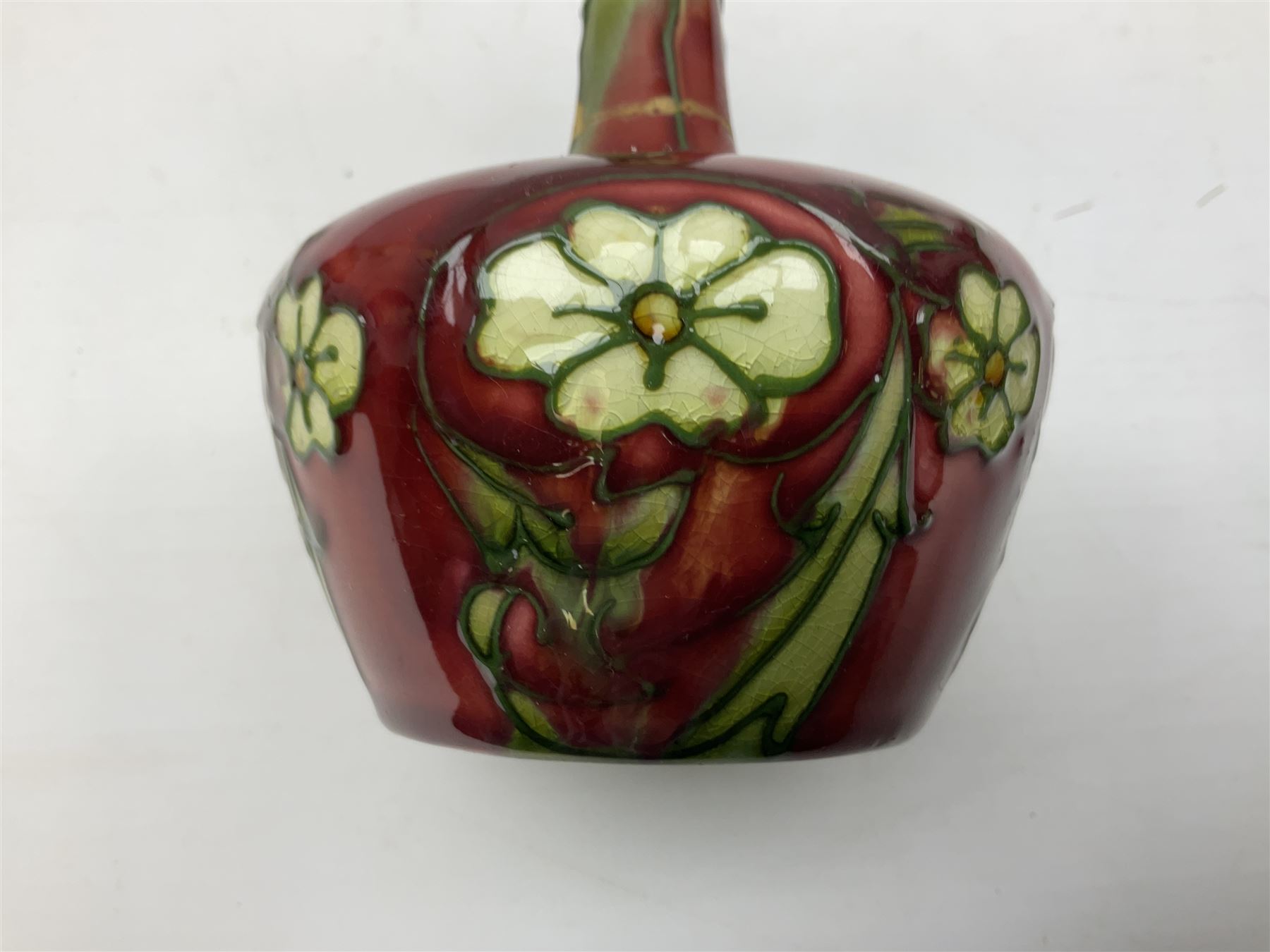 Three Minton Secessionist vases, with tube-lined stylised flower decoration, two upon a red ground and third upon a purple ground, all with printed mark to base 'Minton Ltd, No. 33', H13cm