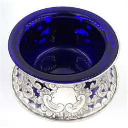 Edwardian silver dish ring in the Irish manner, of circular waisted form, embossed and pierced throughout with flower heads and foliate and C scrolls, hallmarked I S Greenberg & Co, Birmingham 1904, with accompanying blue glass liner, upper rim D17.5cm, approximate weight 6.84 ozt (213 grams)