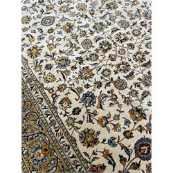Persian Kashan ivory ground carpet, the field decorated with trailing foliate branches and stylised flower head motifs, guarded border with repeating design decorated with scrolling leafy branch and plant motifs 