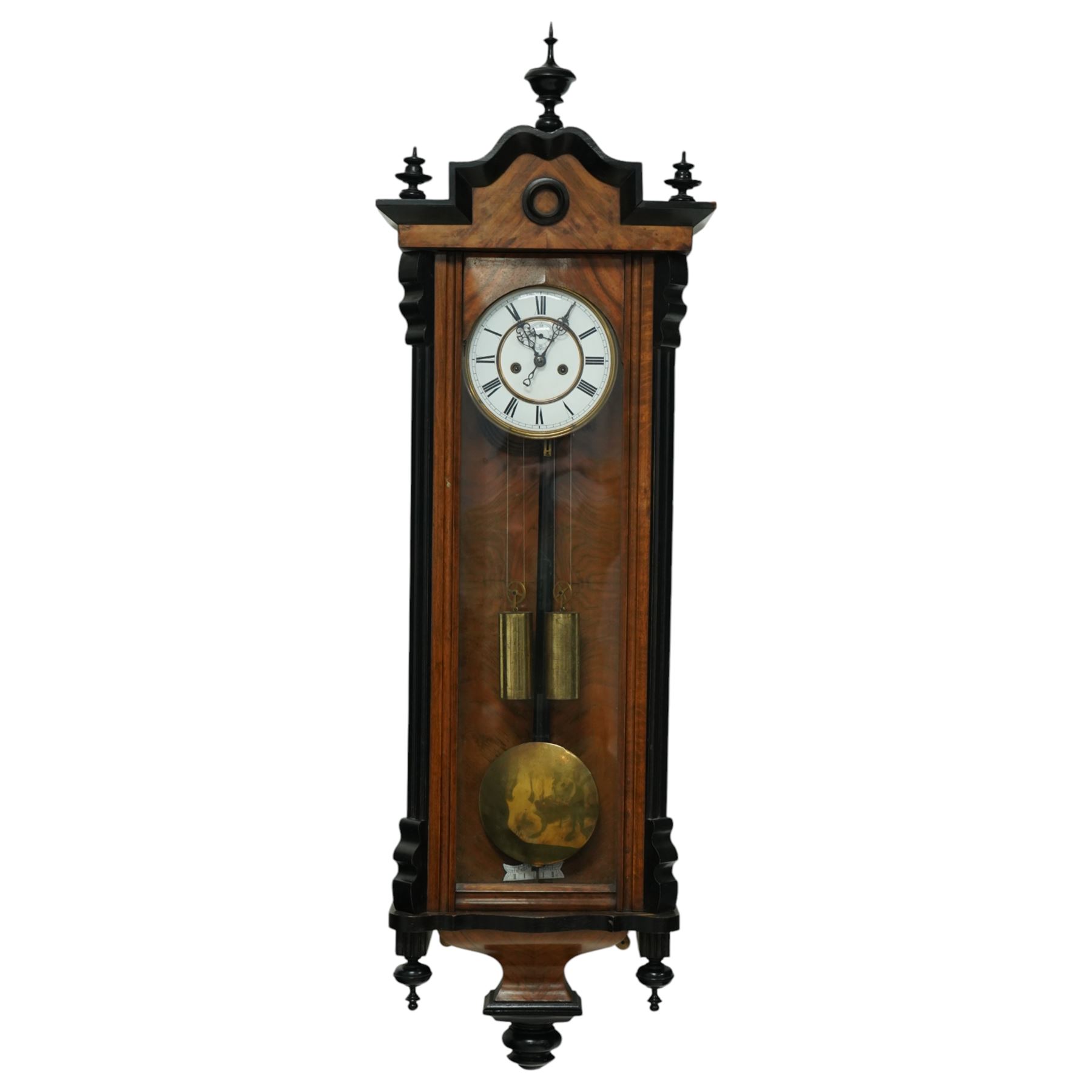 German- Late 19th century twin weight 8-day Vienna wall clock, in a walnut and ebonised case with turned finials and pendants, fully glazed door displaying the the brass cased weights and pendulum, enamel two-part dial with Roman numerals, minute rack, seconds hand and gothic steel hands, rack striking movement with a deadbeat escapement, striking the hours and half-hours on a coiled gong. With key.