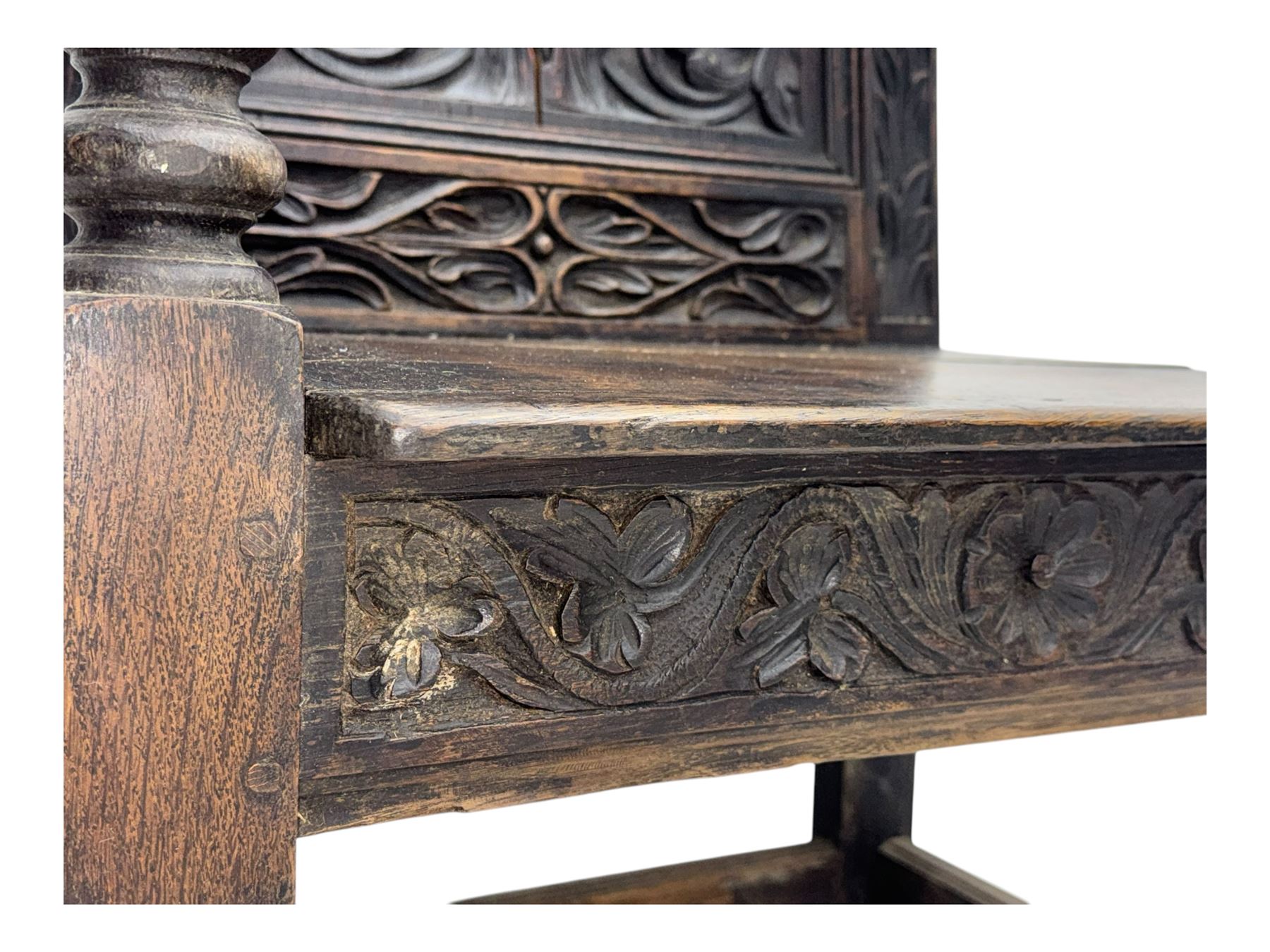 Late 19th century Jacobean revival carved oak armchair, the tall back with arched cresting featuring a stylised foliate mask, flanked by carved scrolls, relief carved panel depicting symmetrical foliage, downscrolled arms, on turned front supports united by stretchers