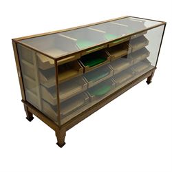 Early 20th century oak framed haberdashery shop counter, glass panel exterior enclosing sixteen graduating drawers with oak fronts and handles, raised on shaped tapering supports 