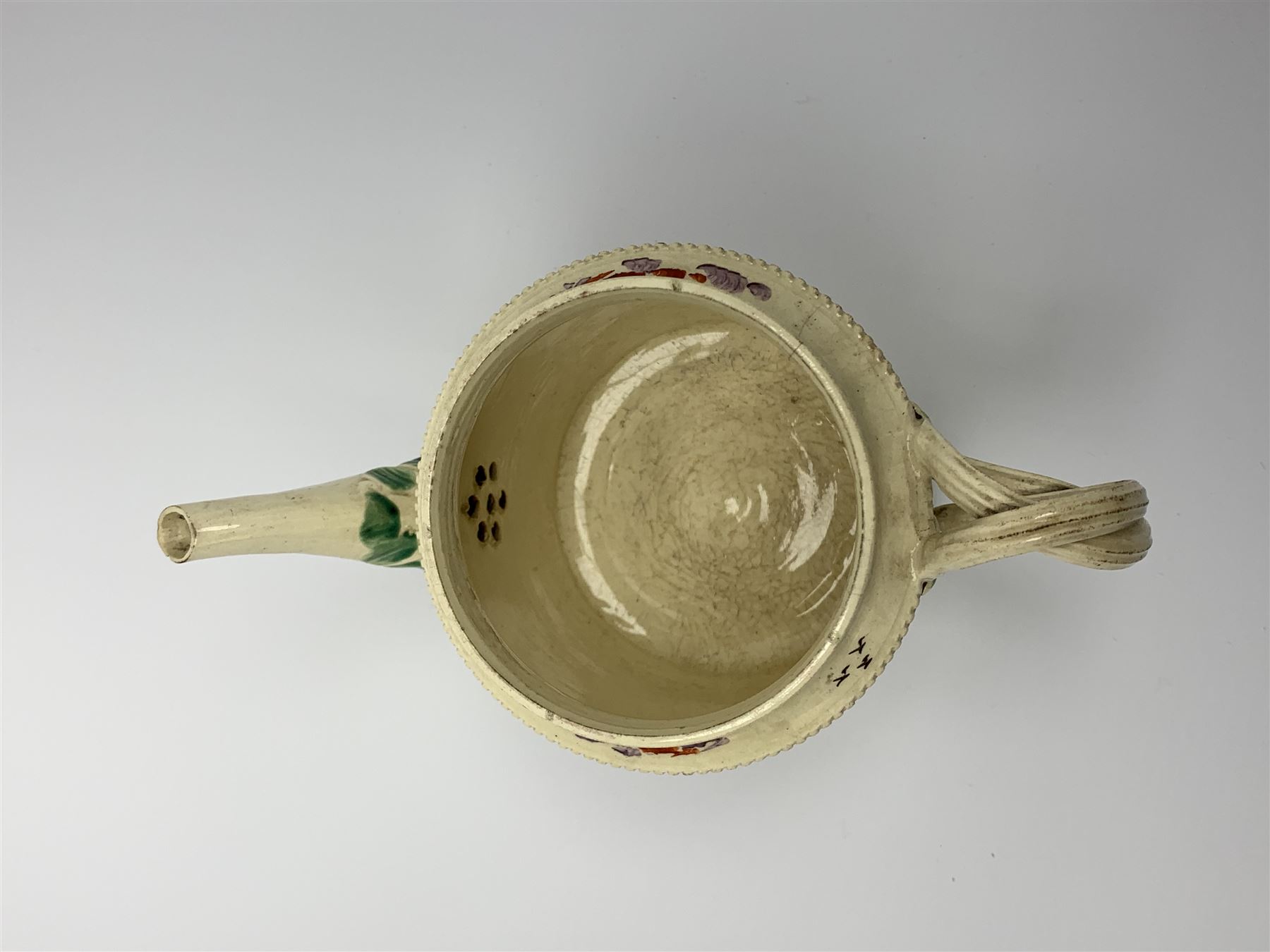 18th century creamware teapot, probably Leeds, with reeded entwined handle and floral finial to the cover, the body with hand painted polychrome decoration of figure to one side, and floral spray to the other, collectors paper label beneath inscribed Leeds Pottery, H11.5cm