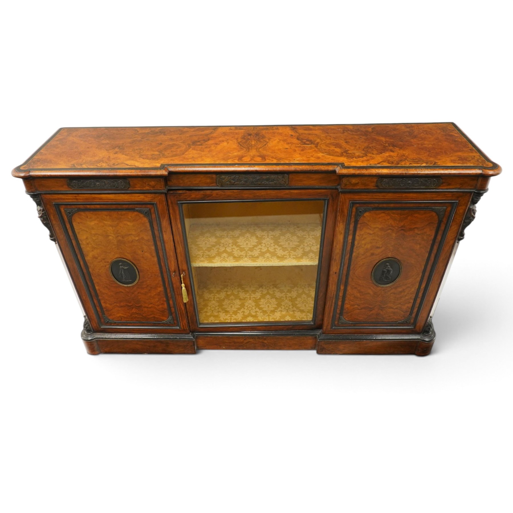 Lamb of Manchester (est. 1843) - Victorian Aesthetic Movement inlaid figured and burr walnut inverted-breakfront credenza, the shaped rectangular top with ebony banding and boxwood stringing, the frieze applied with bronze mounts decorated with foliate and scroll motifs, fitted with central glazed door flanked by panelled doors with central oval metal plaques depicting Classical Muses with lyre, the flanking canted uprights applied with caryatid maidens holding torches, acanthus terminal over skirted base