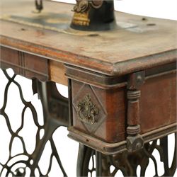 Early 20th century Singer treadle sewing machine, the black enamel machine with gilt floral and scroll transferwork set within a timber cabinet top with folding leaf, raised on cast-iron base with pierced geometric treadle and 'Singer' name stretcher, flanked by two small drawers