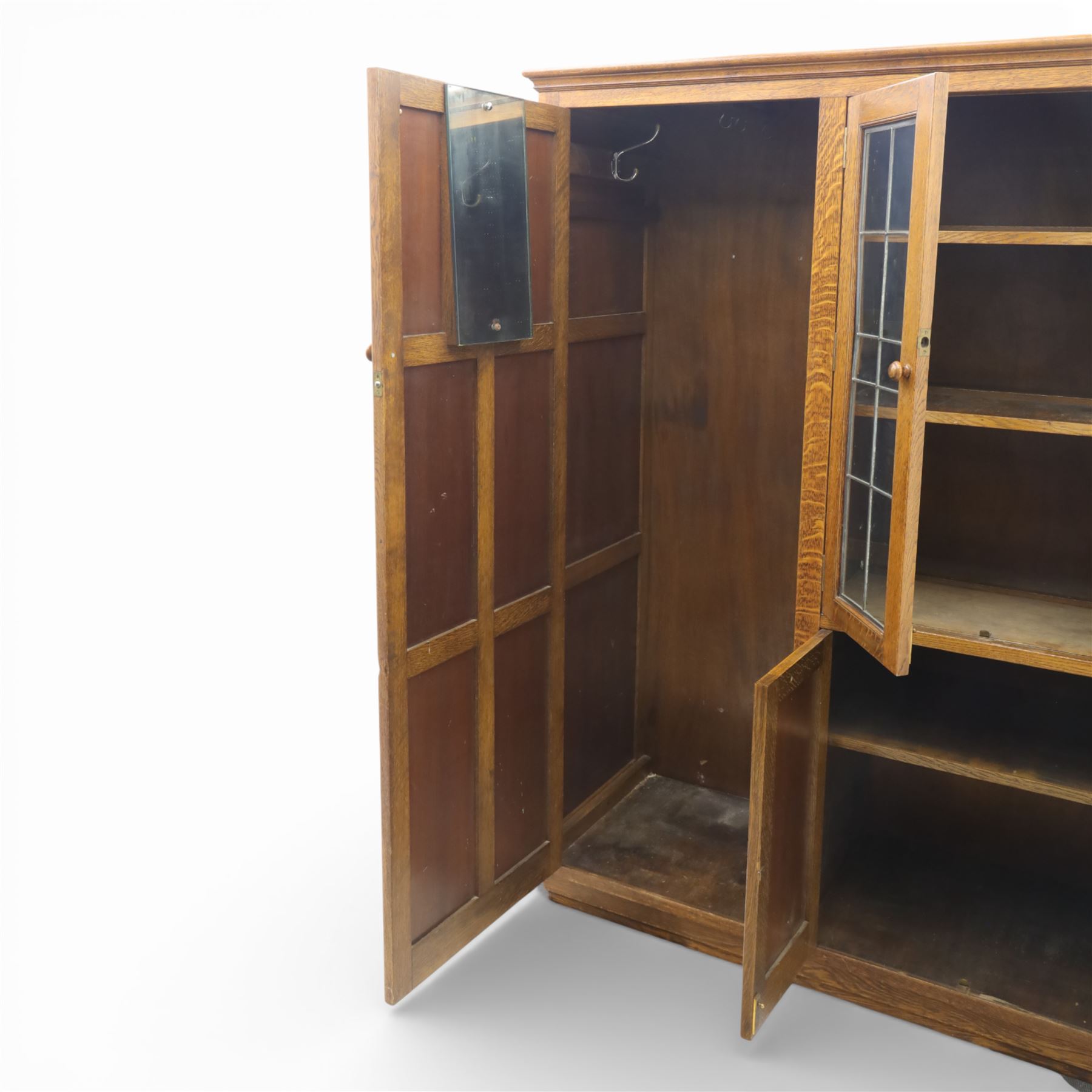 Edwardian oak glazed cabinet, moulded cornice above a panelled front and sides, fitted with lead glazed doors enclosing shelved interior, left side full length cupboard converted to enclose a gun cabinet, on a plain plinth base 