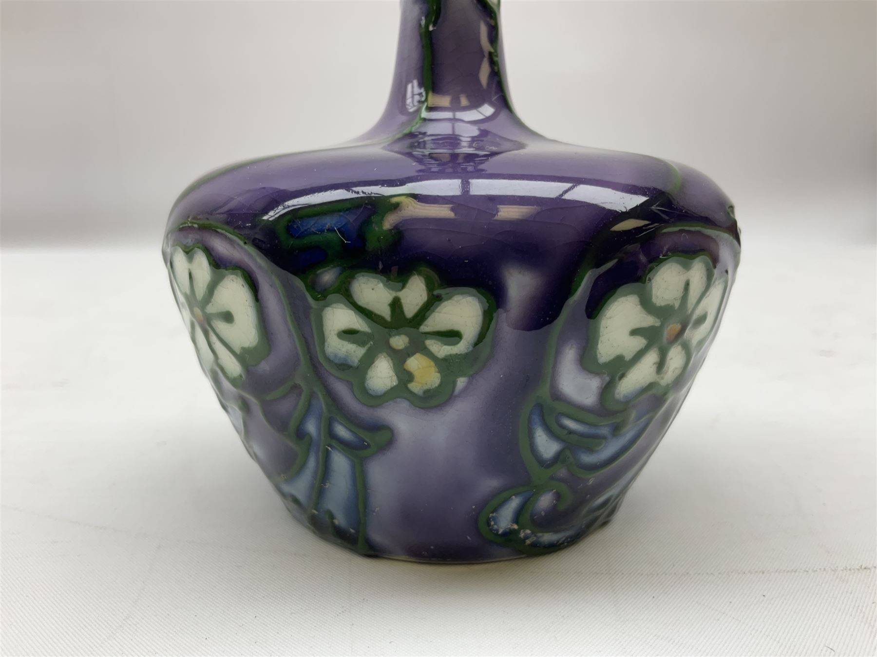 Three Minton Secessionist vases, with tube-lined stylised flower decoration, two upon a red ground and third upon a purple ground, all with printed mark to base 'Minton Ltd, No. 33', H13cm