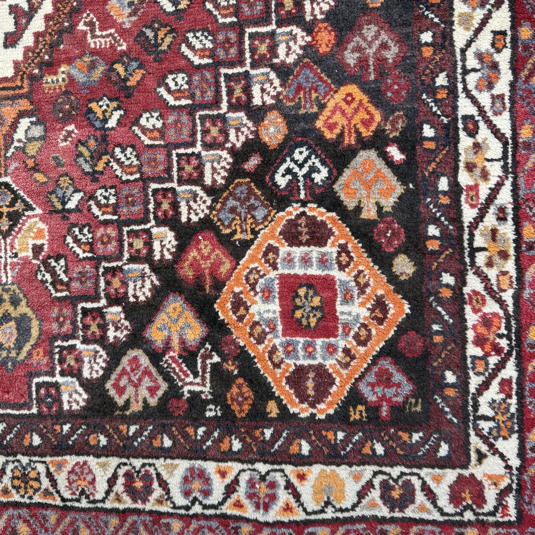 Southwestern Persian Qashqai rug, central diamond medallion with hooked motifs flanked by four corner medallions on a rich red madder field with dark brown ground of stylized floral and animal motifs, and ivory border with alternating floral palmettes and a red main  border with a meandering vine pattern 