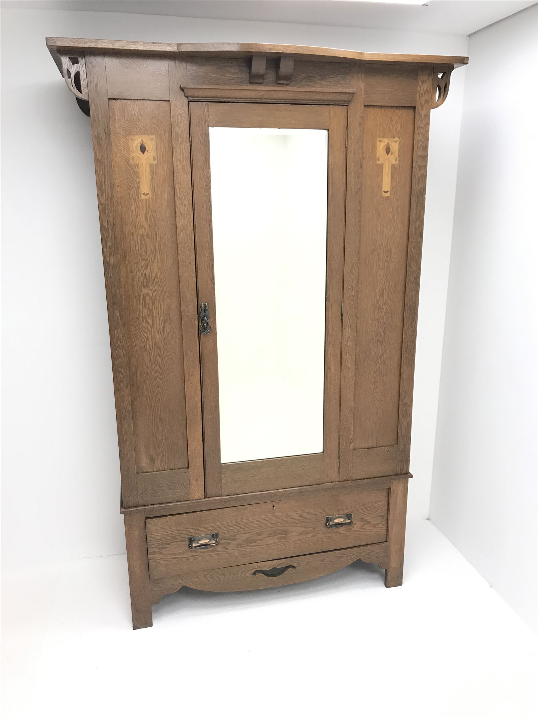Arts and Crafts period oak wardrobe, projecting shaped cornice, single bevel edged mirrored door above drawer