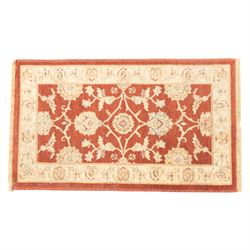 Lot of three Indo-Ziegler style wool rugs, comprising one with central floral medallion and palmette border, and two matching examples with scrolling vine and flowerhead motifs on a deep red field, each with decorative border in soft gold tones (60cm x 85cm) (65cm x 115cm)
