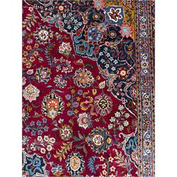 Central Persian Kashan hand-knotted carpet, madder red field with an intricate design of scrolling vines, palmettes, and rosettes with a central lobbed medallion with pendant motifs in shades of blue and ivory, and spandrels all within a blue-ground border of palmettes and flowerheads between multiple guard borders, 450cm x 335cm 