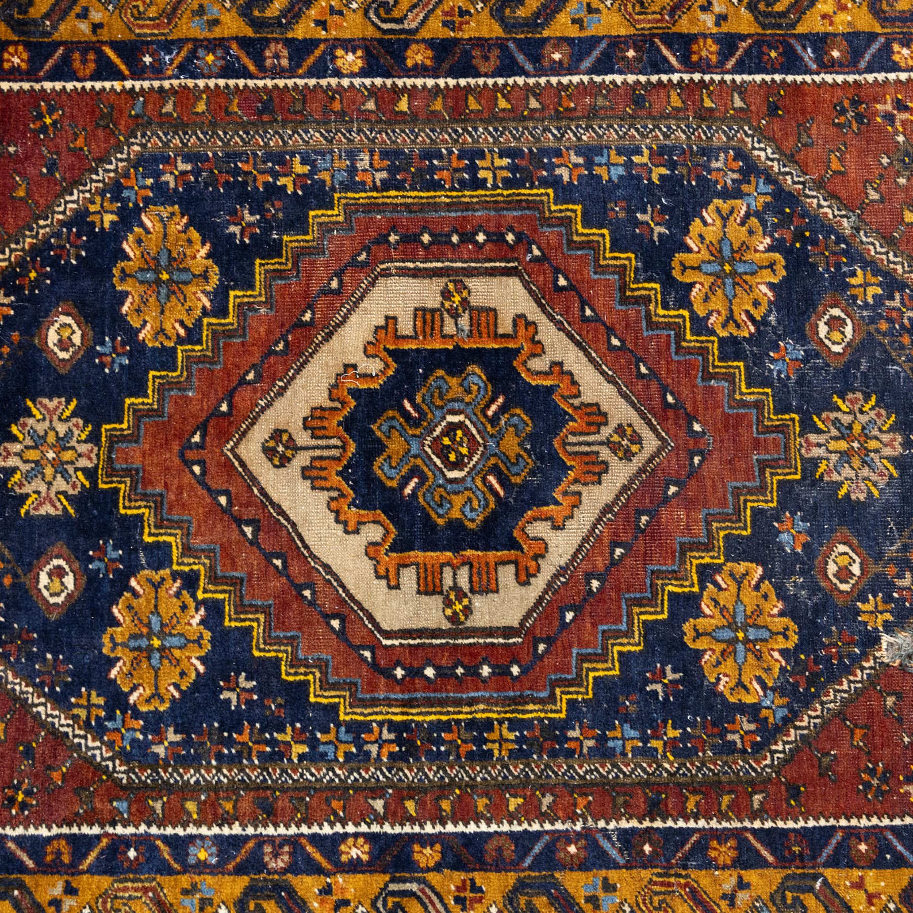 Turkish Anatolian wool rug, central stepped medallion on dark blue lozenge field, red spandrels with stylised hooked motifs, ochre border decorated with repeating geometric motifs and guard stripes