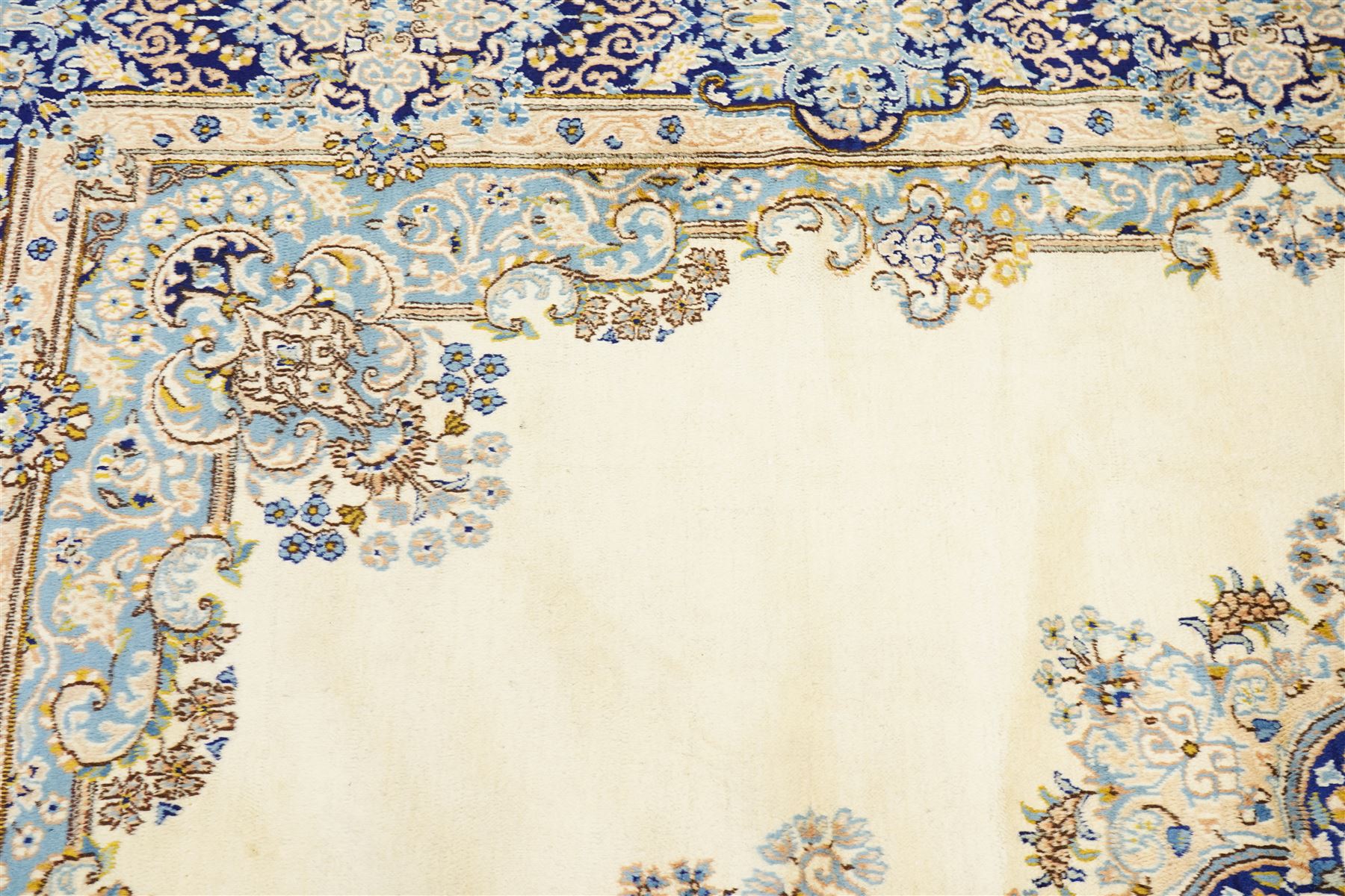 South East Persian Kirman hand-knotted carpet, ivory field with central floral medallion in tones of cobalt and pale blue, issuing scrolling vinery and palmettes, conforming spandrels, main border with scrolling foliage and stylized palmettes, framed by multiple guard borders, with cotton fringe ends 