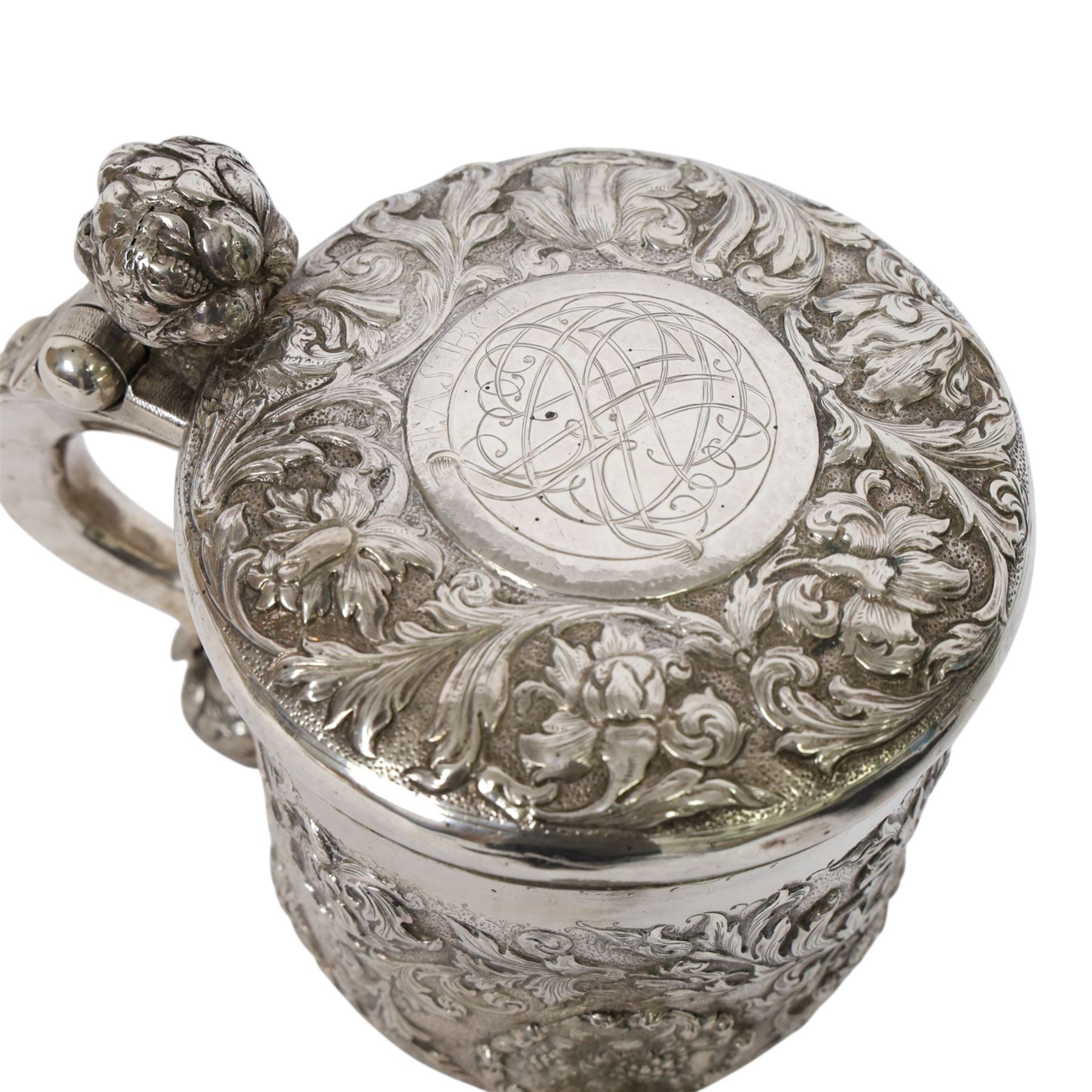 Northern European silver peg tankard, probably late 18th/early 19th century, of cylindrical form, the body repoussé decorated with scrolling and blossoming acanthus, fitted with scroll handle with shield terminal, the hinged cover with conforming repoussé decoration surrounding a central circular panel engraved with monogram beneath initials EASBGD, opening with ball thumbpiece detailed with fruits, raised upon three confirming ball feet mounted with shaped panels also detailed with fruits, bearing indistinct mark beneath, H19cm