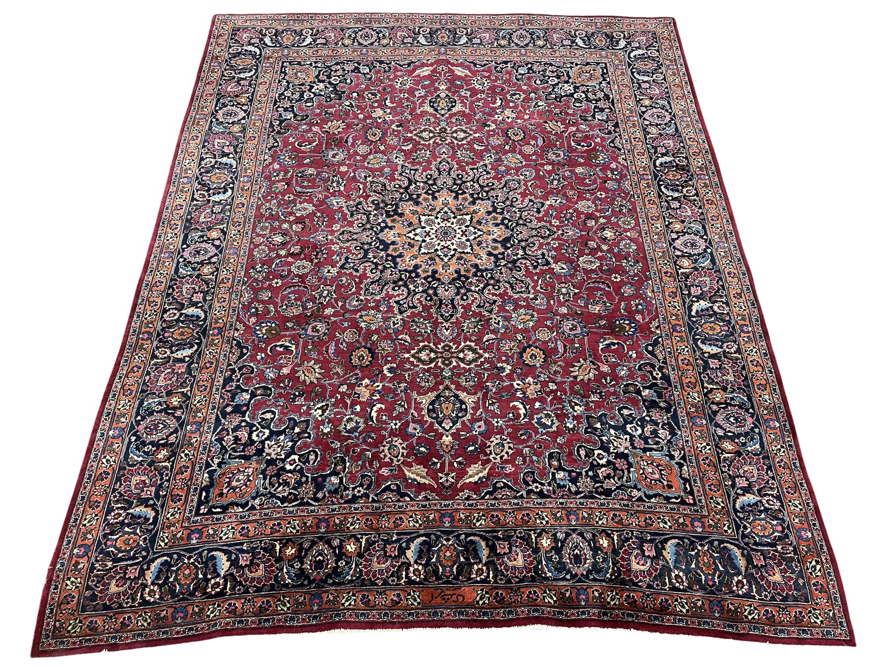 Persian Meshed carpet, plum ground and decorated with stylised flower heads and interlacing foliate, large central stylised medallion with orange detail, the orange mirrored in the five band border decorated with scrolling floral design, signature panel to end 