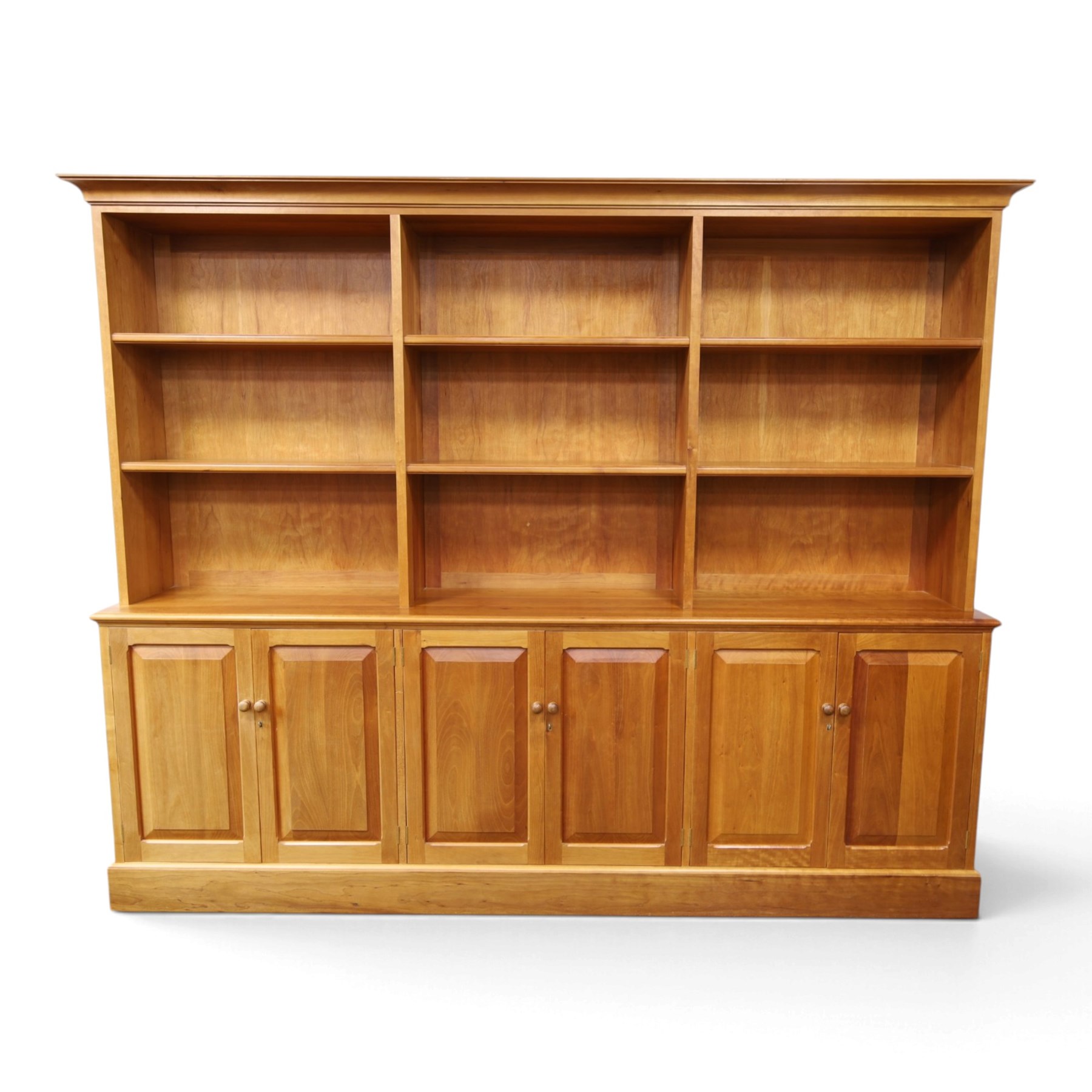 Philip Koomen (1953-) - Craftsman-made modern cherrywood large open
bookcase with a cupboard base, upper section with a
shaped cornice above three sections with two open
shelves, the lower section has three cupboards,
each with two panelled doors enclosing a single
shelf, raised on a plinth base