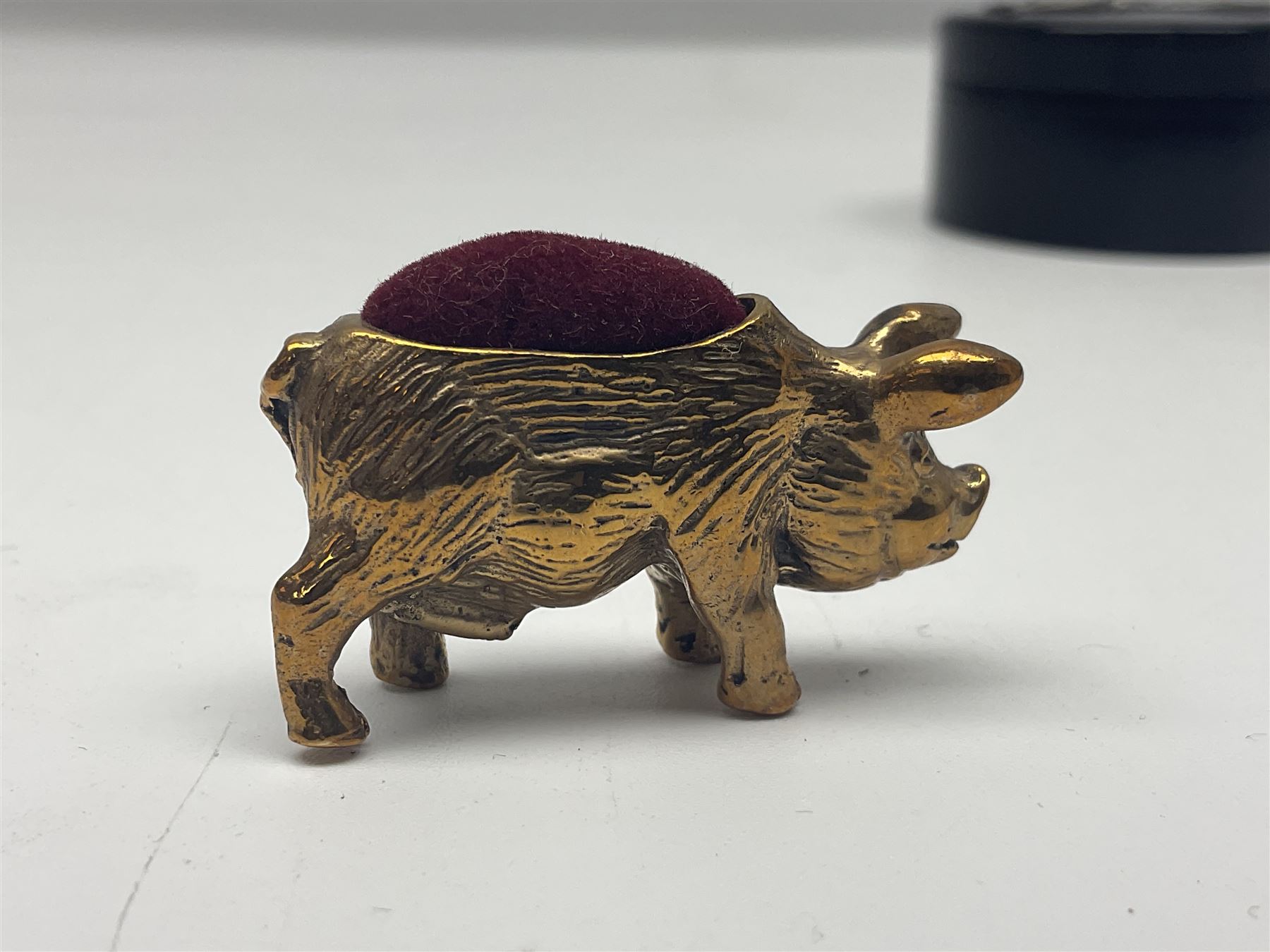 Three pin cushions, comprising gilt metal pig, silver plate shoe, circular pin cushion on threel feet, together with black pin holder with silver writing to the lid 