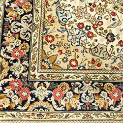 Central Persian Kashan hand-knotted carpet, ivory ground, with an all-over floral field centred by a subtle shaped medallion, surrounded by scrolling foliate and floral motifs incorporating rosettes, palmettes and delicate vine work, enclosed by a dark navy border with repeating palmettes and meandering vines, flanked by floral guard stripes, with cotton fringes