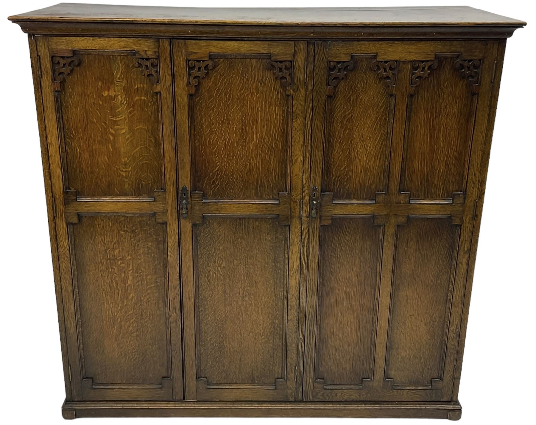 Early 20th century oak triple wardrobe, three panelled doors with geometric mouldings and fretwork spandrels, the interior fitted with slides and hanging rail