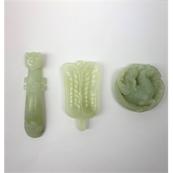 A carved celadon jade belt hook, L9.5cm, together with a celadon jade disc with carved zoomorphic detail, D5.5cm, and a carved celadon jade pendant of stylised naturalistic form, H7.5cm. (3). 