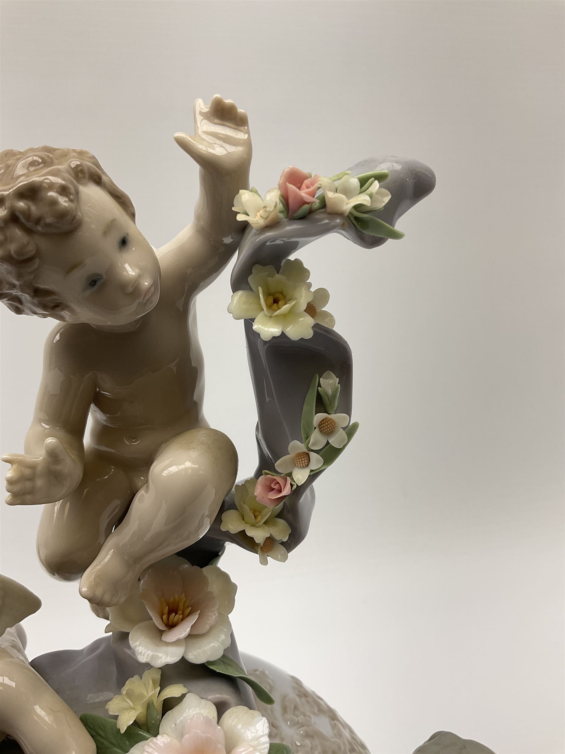A Lladro mantel clock modelled as a globe with inset clock, surmounted by four putti and floral garlands, with blue printed mark and impressed 5973 beneath, H29cm.