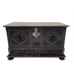 Early 20th century carved hardwood kist or mule chest of small proportions, moulded rectangular hinged lid over foliage carved geometric lozenge panels, the frame carved with chevron banding, fitted with two drawers, the drawer fronts carved with extending leaf motifs over a foliage carved lower moulding, on turned feet