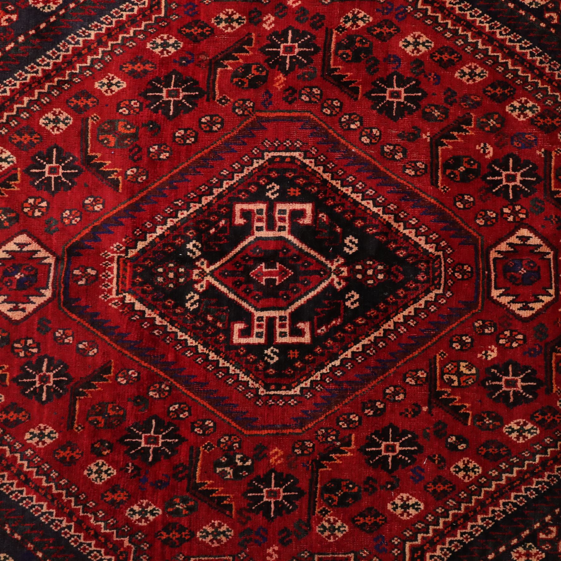 South West Persian Qashqai hand-knotted rug, madder red field with a large stepped diamond medallion with scattered geometric devices and indigo spandrels filled with geometric motifs, framed by multiple narrow guard borders and broad main border, wool fringe ends 