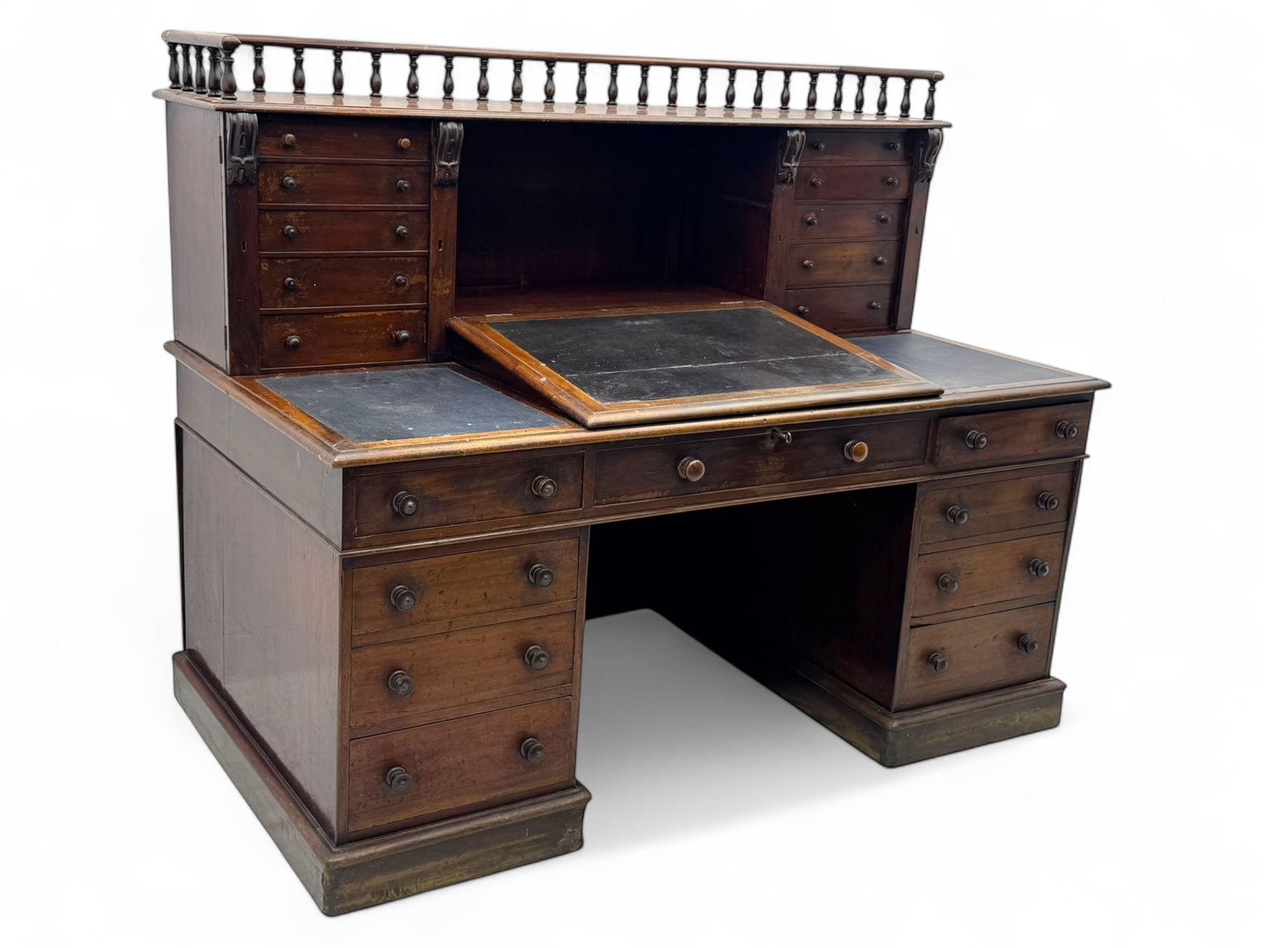 Large Victorian mahogany Registry/Dickens’ desk, spindle gallery top, one side with five small drawers and the other with blind cupboard drawer, revealing pigeon holes with scroll carved locking side bars on either side, above a hinged and leathered writing slope with three drawers and pigeon holes underneath, above a central locking drawer with key, the pedestals each with four drawers and  turned knob handles, separates into four parts for transport
