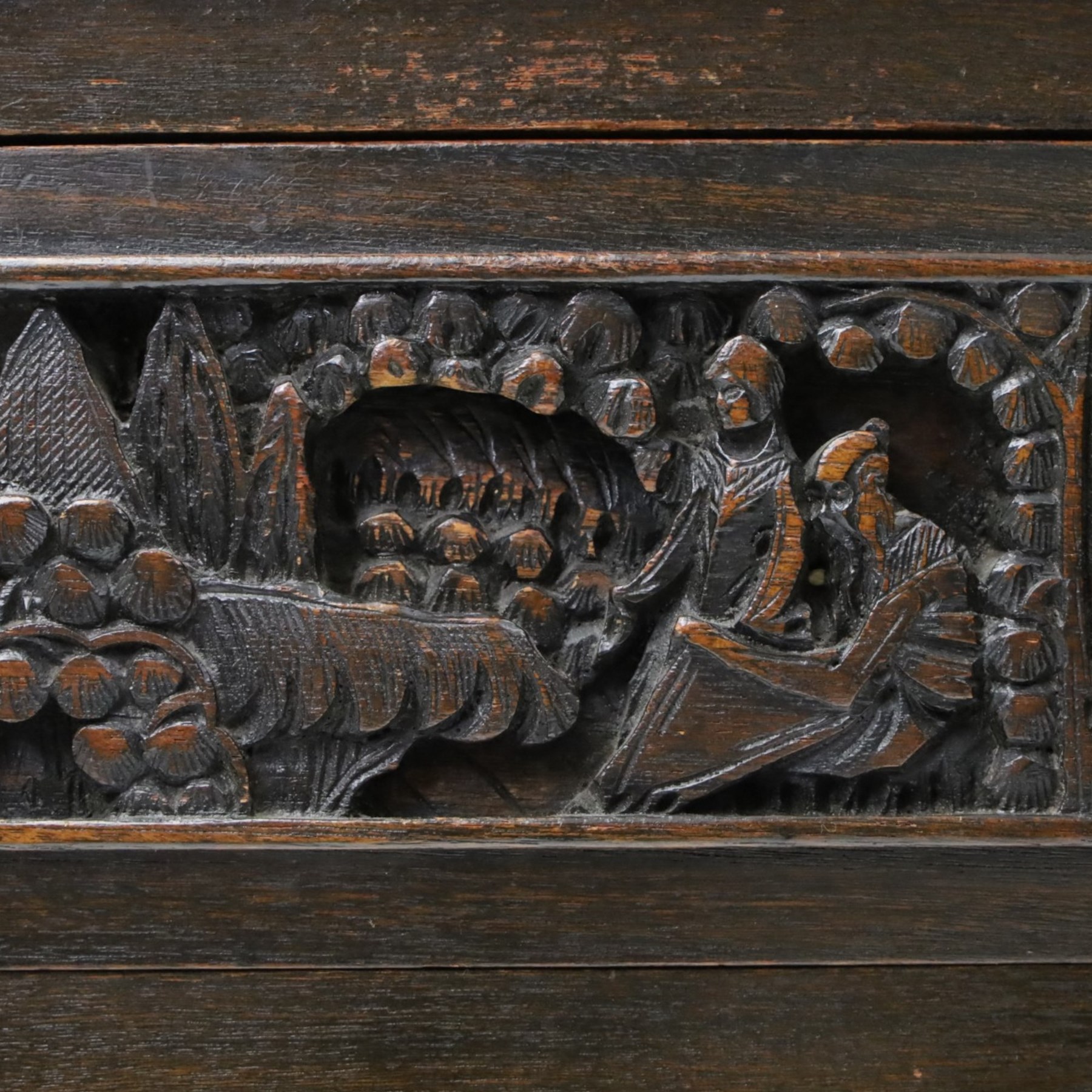Early 20th century Chinese export carved hardwood writing bureau, the sloped fall front deeply carved with a narrative figural scene beneath pine and prunus trees, above a pair of rectangular carved panels, the shaped crest rail with entwined dragons, interior fitted with pigeonholes and a central drawer, on figural front supports with shaped stretcher
