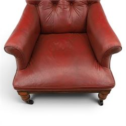 Early 20th century style oxblood red leather Chesterfield armchair, deep buttoned shaped back over padded scroll arms and loose seat cushion, raised on turned mahogany front supports with brass caps and castors