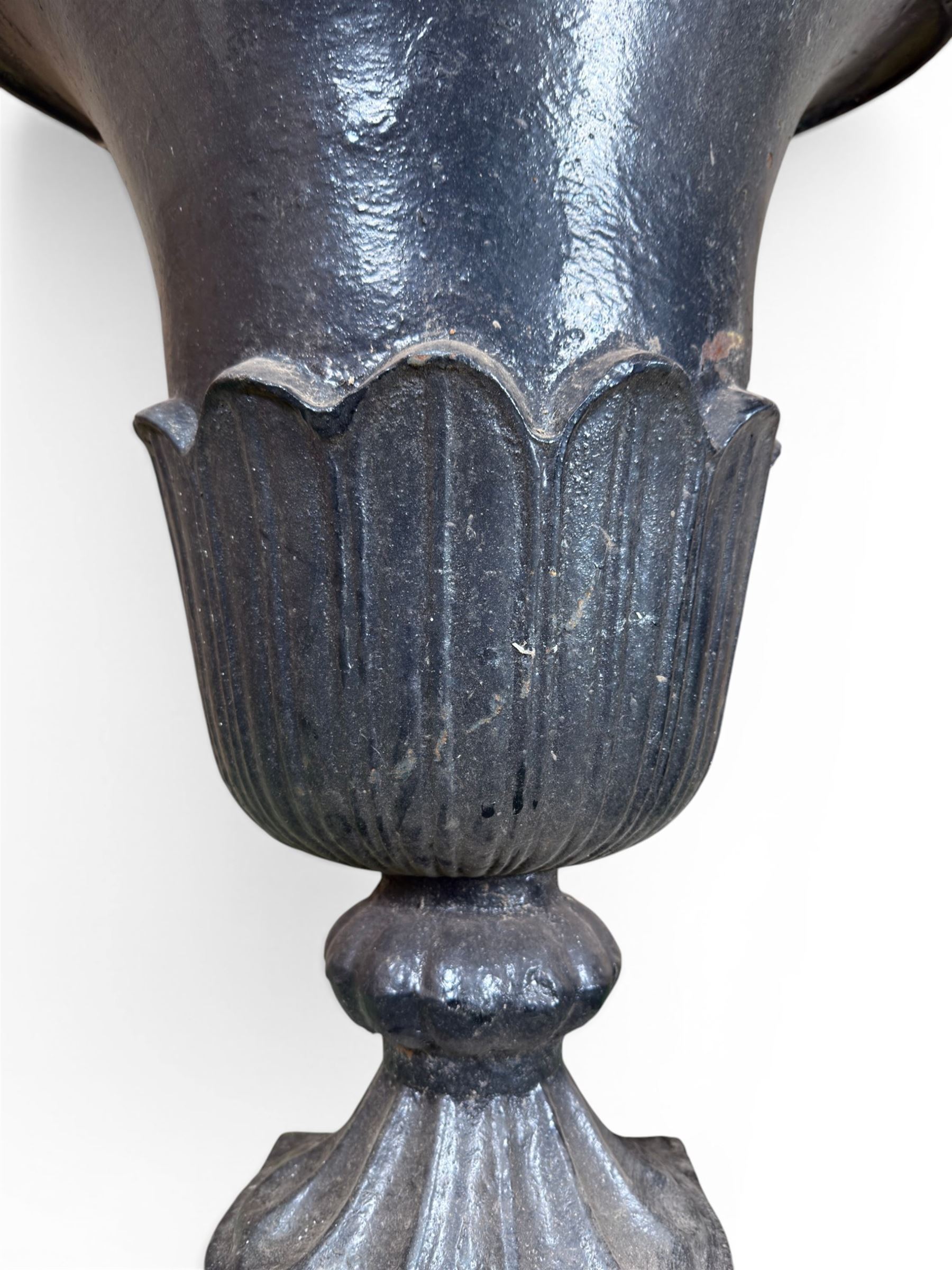Pair of Victorian large scale cast iron garden urns, flared petal shaped rim with tapering waist, gadrooned base on square plinth, finished in black paint