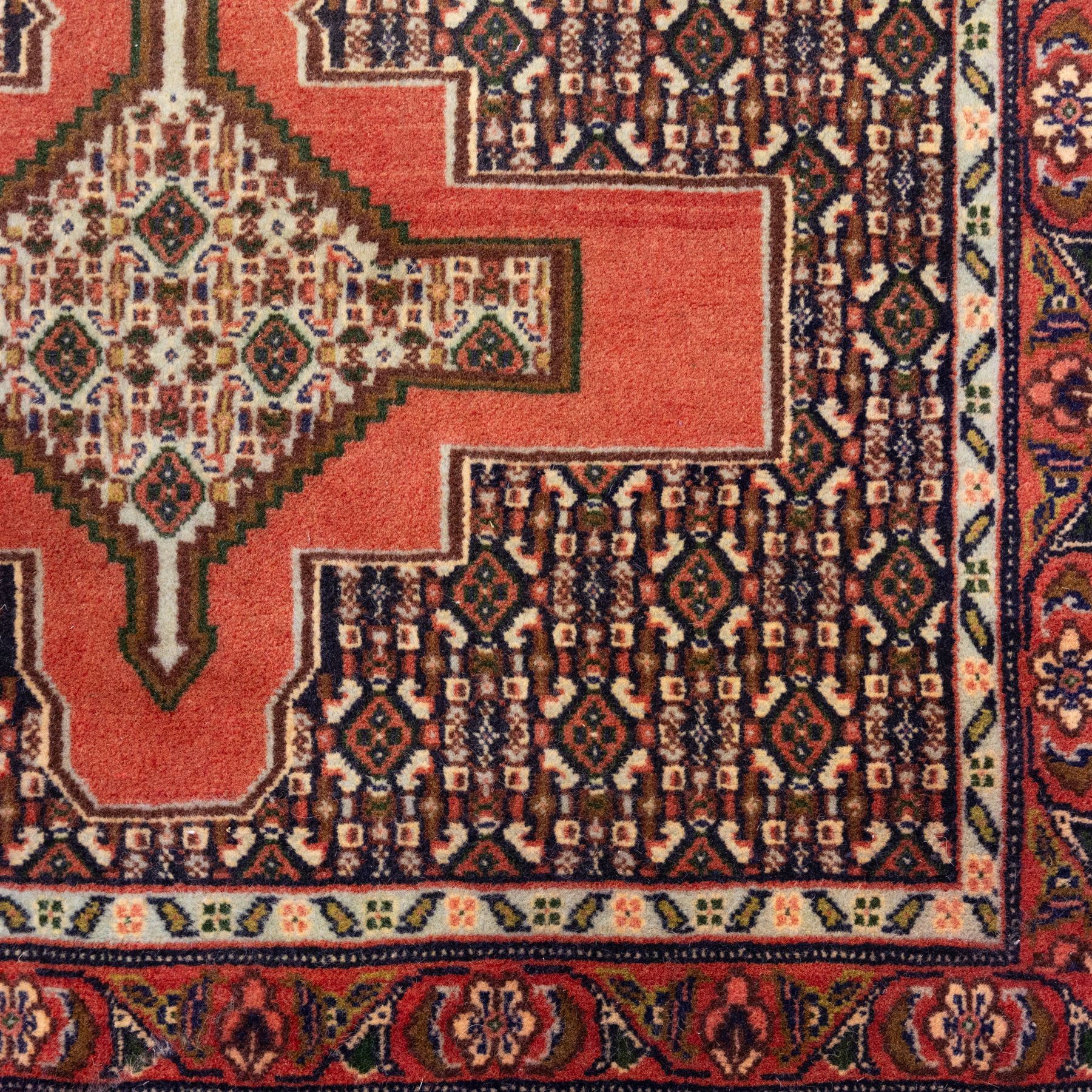 North West Persian Senneh hand-knotted runner, decorated with a continuous series of stepped and hooked geometric medallions against a madder red ground, enclosing herati style and small geometric floral motifs, framed by a principal border and flanked by multiple narrow guard stripes, with cotton fringe ends 
