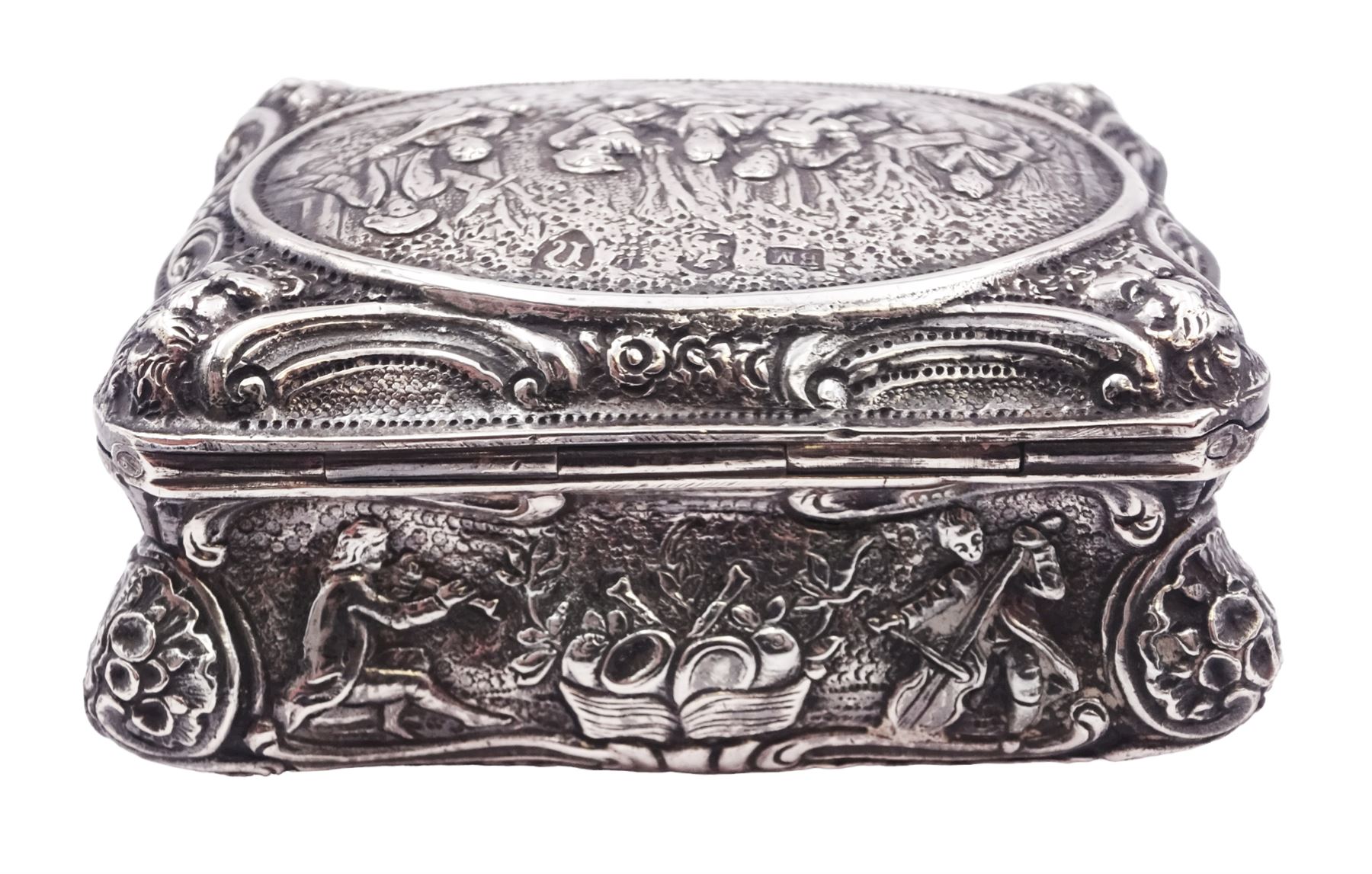 Late 19th century German Hanau silver box, of shaped rectangular form, embossed throughout, the hinged cover decorated with a central oval panel depicting a genre scene with musicians, the corners detailed with masks, the sides detailed with conforming figures and musical trophies, opening to reveal a gilt interior, with Hanau marks for Neresheimer & Sohne, and hallmarked B Muller & Son, London import 1907, approximate weight 3.32 ozt (103.4 grams)
