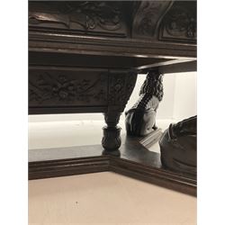 Large 19th century carved oak library table, the rectangular top with lunette carved edge over cartouche panelled and carved  scroll frieze, the central tapering rectangular support relief carved with masks and garlands, on four carved seated lion supports at each corner, on flat angular stretcher with recessed castors stamped ‘Bartholomew & Fletcher, London’