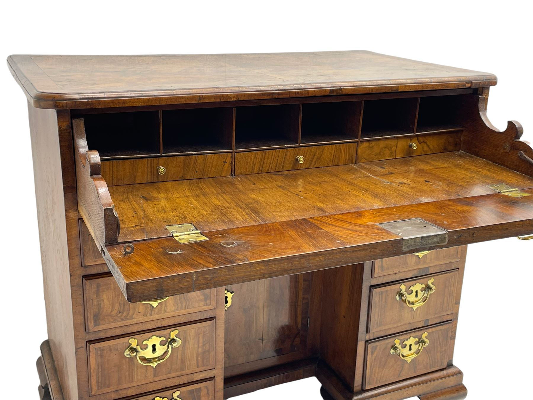 Early 18th century Queen Anne figured walnut kneehole desk with secretaire drawer, moulded and book matched top with walnut band, the top drawer with fall front enclosing small drawers and pigeon holes, fitted with nine drawers and central recessed cupboard, on ogee bracket feet