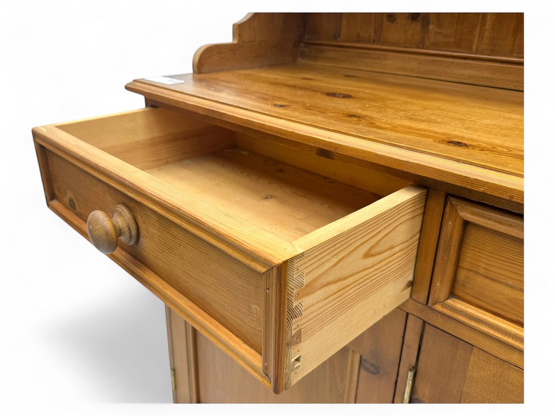 Traditional vintage pine kitchen dresser with scrolled cornice and rack with long shelf above a galleried shelf flanked by three short drawers and two cupboards, the base with three long drawers above three cupboards on plinth base  