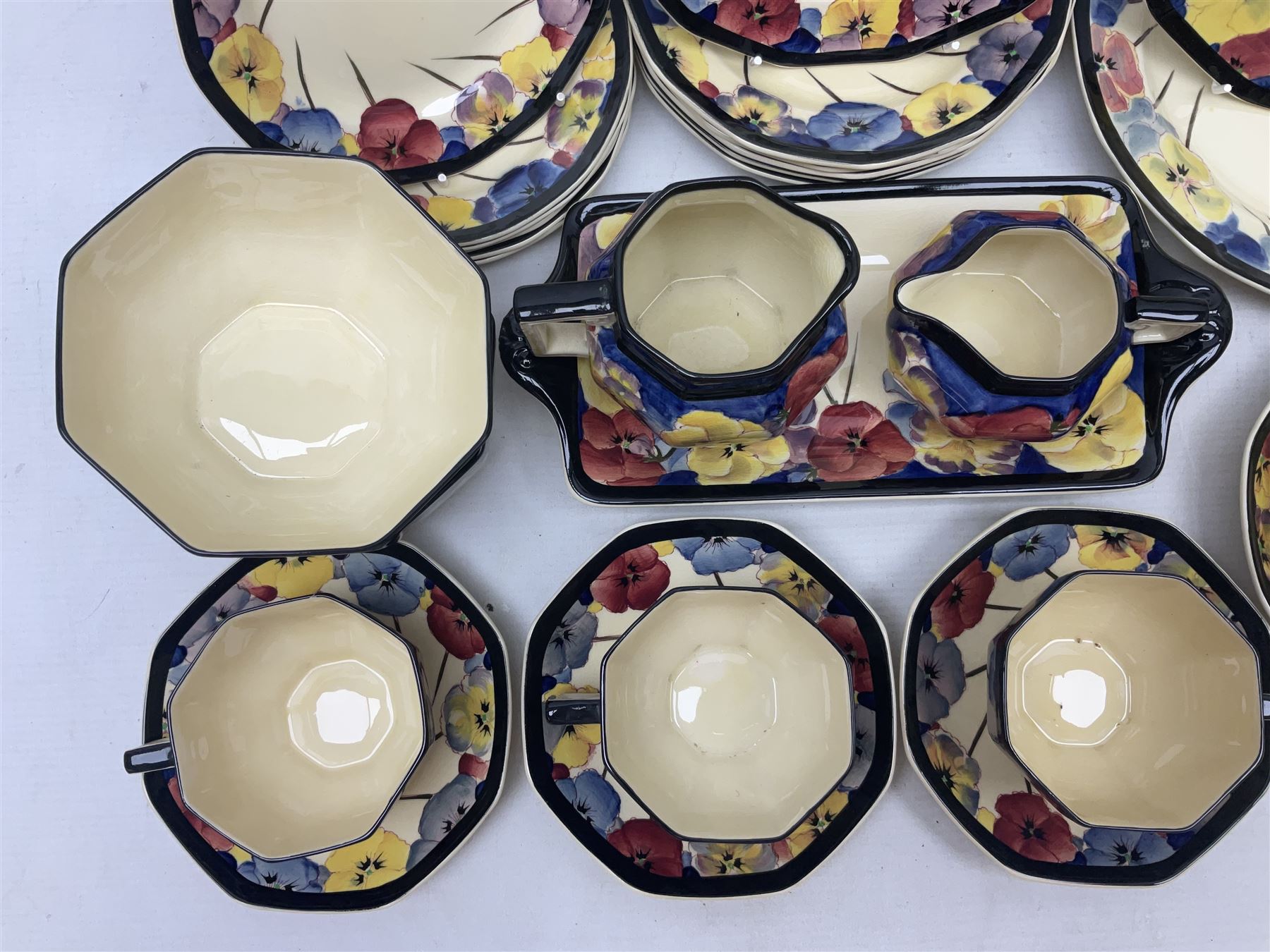 Early 20th century Art Deco Royal Doulton Pansies pattern octagonal teawares, comprising three larger teacups and saucers, three smaller teacups and saucers, open sucrier, two jugs, slop bowl, six side plates, two larger plates, two small circular dishes and one long twin handled rectangular dish, all with printed marks beneath, Rd No 597783, pattern no D4049