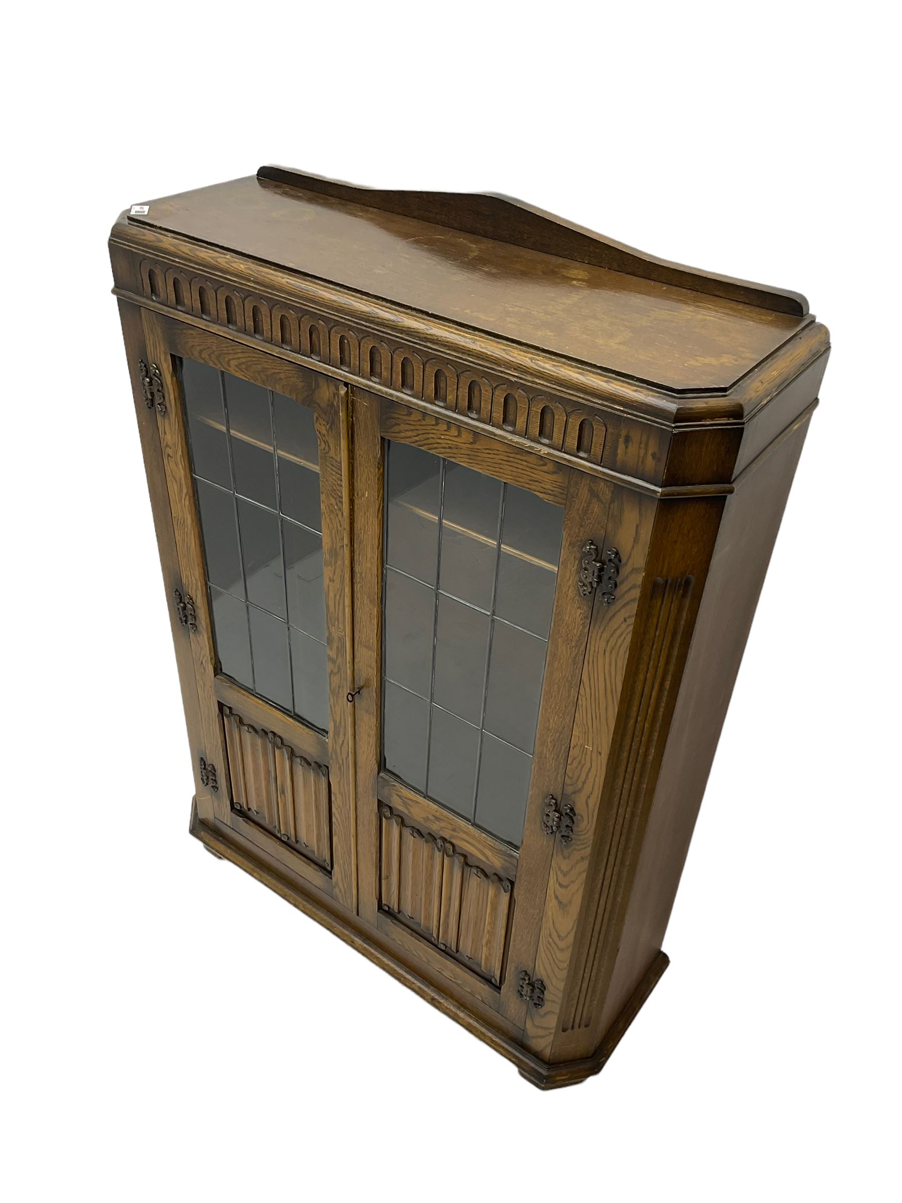 Oak bookcase enclosed by glazed doors with linenfold panels