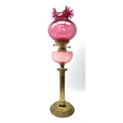 A Victorian oil lamp, the brass base with circular stepped foot supporting a Corinthian modelled column, with cranberry glass burner and frilled cranberry glass shade and clear glass chimney, (converted for electric), H75cm.